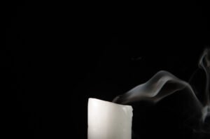 Burning candle with fading flame and smoke on a black background